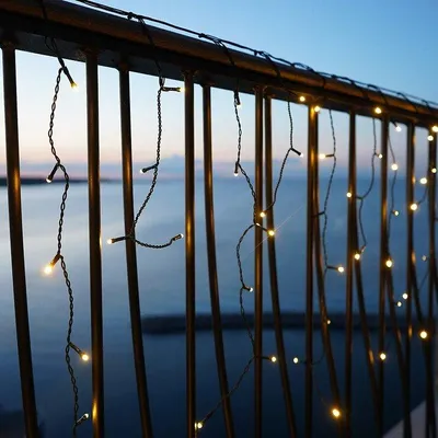 String lights hanging on a balcony railing overlooking the water at dusk.