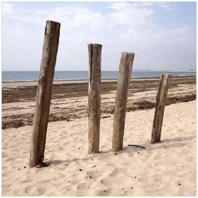 Produktbild von Wallario Wandbild aus Acryl, 50 x 50 cm, freischwebende Optik - Sandstrand mit Holzpfählen am Atlantischen Ozean