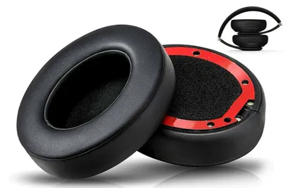Two black headphone ear pads are shown on a white background. One ear pad is in focus and angled towards the viewer, while the other is partially visible behind it and shows the adhesive backing with red tape. A small inset image in the upper right corner 