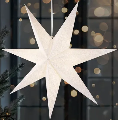 A white star-shaped lantern hangs in front of a window with blurred lights.