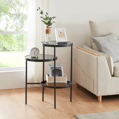 A three-tiered black metal side table with glass tops, placed next to a sofa in a living room.