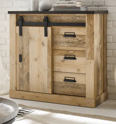 A wooden sideboard with a sliding barn door and drawers, set against a white brick wall.