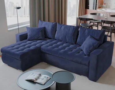 A blue sectional sofa is shown in a living room setting with a window and curtains in the background.