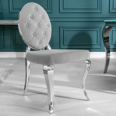 A close-up of a gray velvet dining chair with tufted back and silver legs, set against a teal wall.