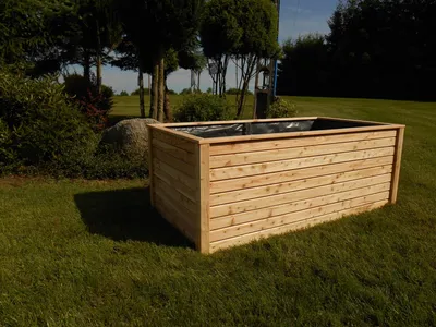 A wooden raised garden bed sits on a grassy lawn with trees and bushes in the background.