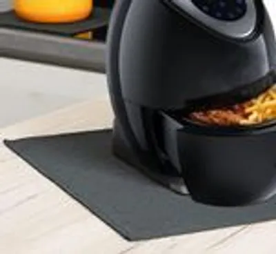 Close-up of a black air fryer on a grey mat on a wooden surface. Some food is visible in the air fryer basket.