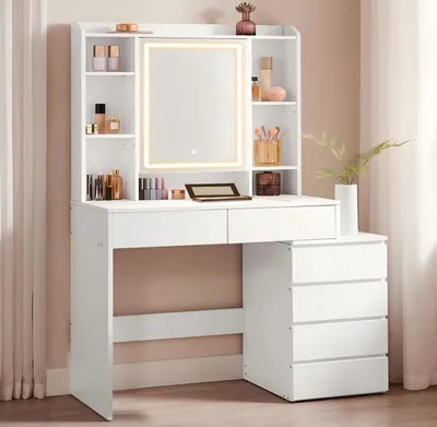 A white vanity table with a lighted mirror and drawers, set against a light pink wall.