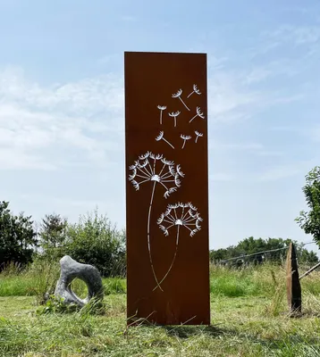 A tall, rectangular metal garden decoration with a dandelion motif is placed in a grassy outdoor setting.