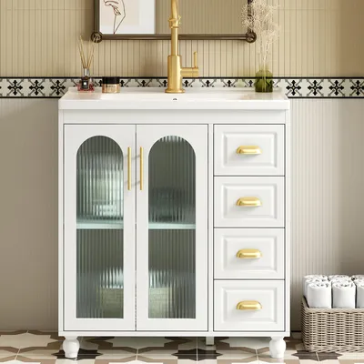 A white bathroom vanity with a gold faucet and gold hardware, set against a tiled wall.