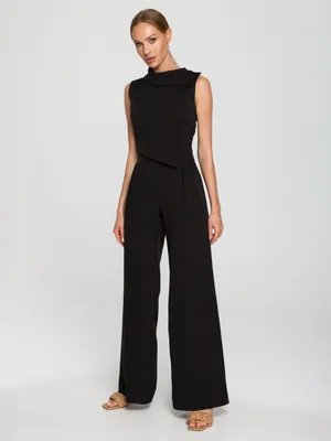 A woman wearing a black jumpsuit stands against a white background.