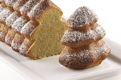 A Christmas tree shaped cake, dusted with powdered sugar, on a white platter.