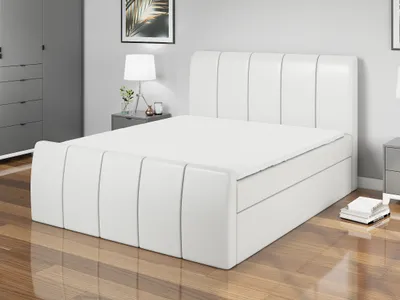 A white boxspring bed with a mattress and topper is shown in a bedroom setting.