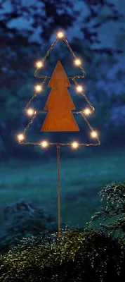 A decorative Christmas tree stake with lights in a garden at night.