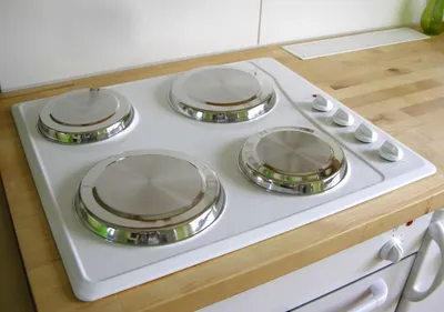 A close-up shot of a white electric stove top with four silver heating elements, placed on a wooden countertop.