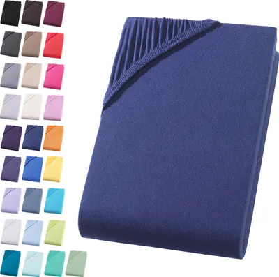A folded dark blue fitted sheet is shown on a white background, with a collage of other colored fitted sheets arranged to the left.