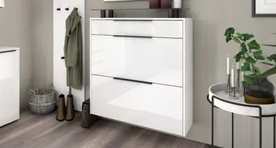 A hallway with a white shoe cabinet, a coat rack with a green coat, and boots.