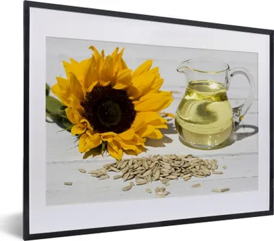 Produktbild von MuchoWow® MuchoWow® Gerahmtes Poster Sonnenblumenkerne mit Sonnenblumenöl in einem kleinen Glas und Sonnenblume auf einem weißen Tisch 40x30 cm - Poster mit zchwarzem Bilderrahmen - Bilderrahmen - Pos