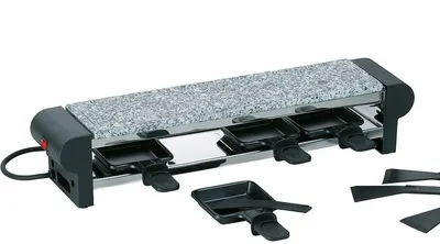 A raclette grill with a stone top and four individual cooking pans underneath, along with several spatulas.