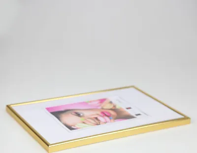 A gold-colored picture frame with a photo of a woman's face inside, lying on a white surface.