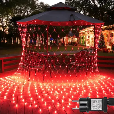 Red net lights are draped over a gazebo and spread across a wooden deck, with a house decorated for Christmas in the background.