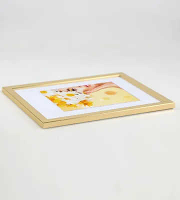 A gold picture frame with a white mat and a collage of images inside, placed on a white surface.