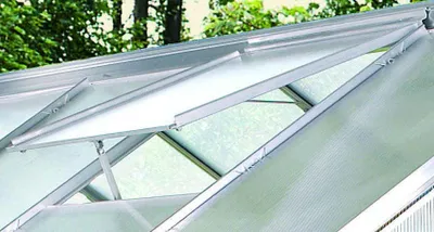 Close-up view of an open greenhouse roof window with aluminum framing and translucent panels.