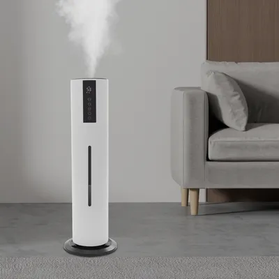 A white humidifier emitting mist in a modern living room setting next to a grey sofa.
