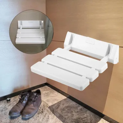 A white foldable shower seat mounted on a wall, with a pair of brown shoes on the floor below.