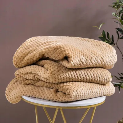 A stack of folded beige blankets on a white and gold side table, with a plant in the background.