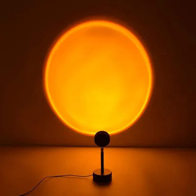 A sunset lamp projects a large orange circle onto a wall, with the lamp itself visible in the foreground.