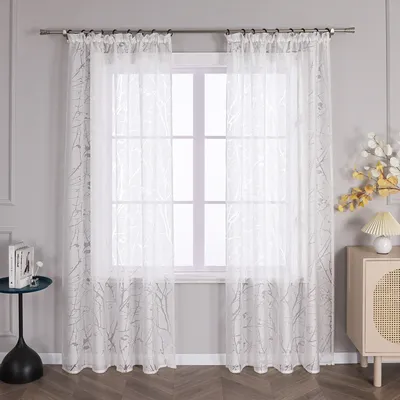 A pair of white sheer curtains with a subtle gray floral pattern hanging in front of a window.