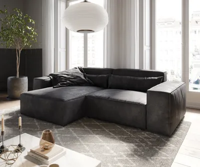 A modern living room with a dark gray sectional sofa, a large potted plant, and a white pendant light.