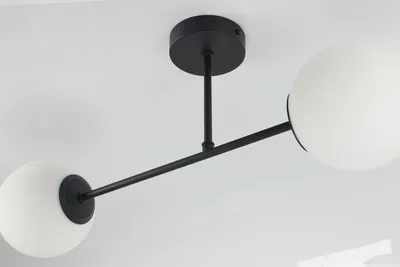 A close-up shot of a modern black ceiling light with two white glass globe shades, mounted on a white ceiling.