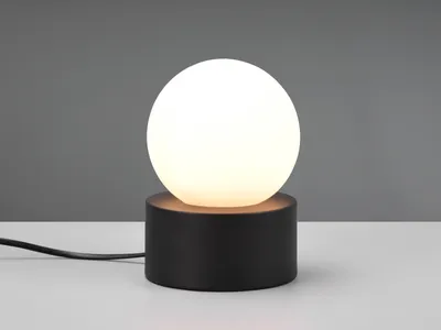 A modern black table lamp with a white globe light sits on a white surface against a gray background.
