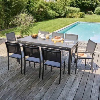 A dining set with chairs and a table is set up on a wooden deck next to a swimming pool.