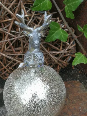 A decorative Christmas bauble with a deer head ornament, set against a natural background of twigs and ivy.