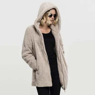 A woman wearing a beige sherpa jacket and sunglasses, posing against a white background.