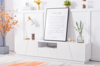 A white TV stand with various decorative items on and around it, set against a white paneled wall.