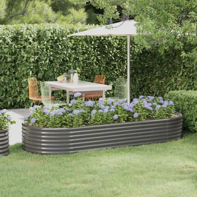A raised garden bed filled with purple flowers in a garden setting, with a table and chairs under an umbrella in the background.
