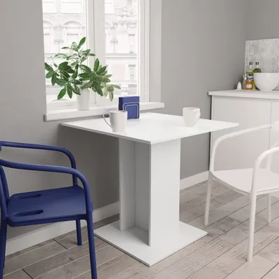A white dining table with two chairs in a room with a window.