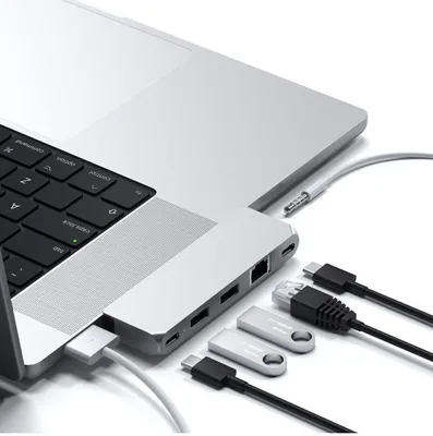 A close-up view of a laptop with a silver docking station attached, showing various ports and connected cables and USB drives.