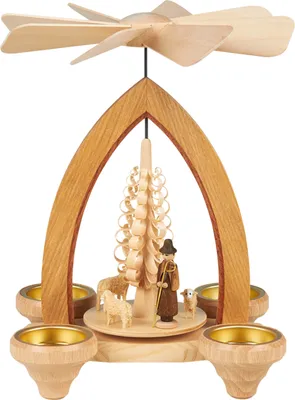 Das Bild zeigt eine hölzerne Weihnachtspyramide mit einem Schäfer und Schafen um einen Baum herum sowie vier Teelichthaltern und einem Propeller an der Spitze
