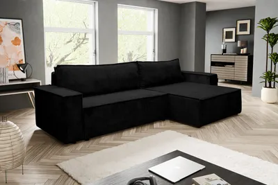 A modern living room with a black sectional sofa, a coffee table with a laptop, and large windows.
