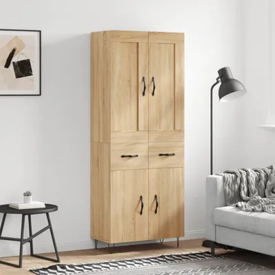 A tall, narrow wooden cabinet with multiple doors and drawers stands against a white wall. A black side table with a book and a small plant is to the left, and a floor lamp and part of a sofa are to the right.
