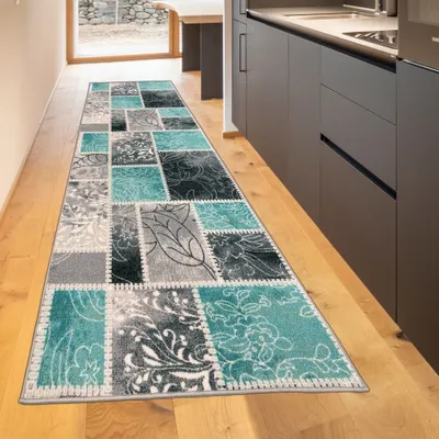 A long runner rug with a patchwork design in turquoise, gray, and cream colors is laid out on a wooden floor in a hallway or kitchen area.