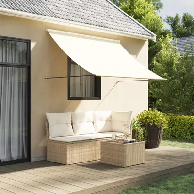 A patio awning is extended over a wicker sofa and coffee table on a wooden deck, with a garden and trees in the background.
