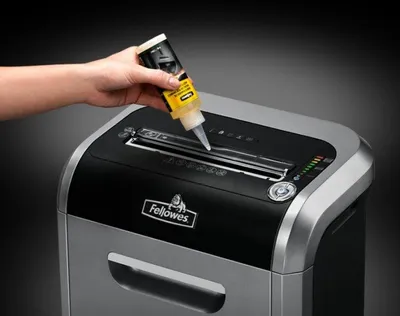 A hand is applying oil to a paper shredder.