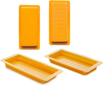 Four orange nougat molds are displayed against a white background. Two are shown from a top-down perspective, one with a smooth surface and the other with a grid pattern. The other two are shown from a diagonal perspective, revealing their shallow, rectang