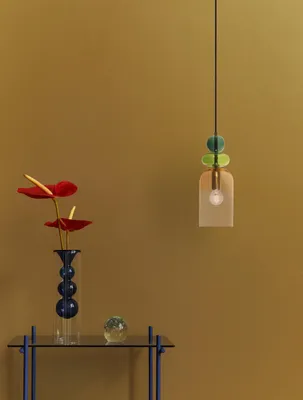 A modern pendant light hangs above a glass table with a vase of flowers and a decorative sphere.