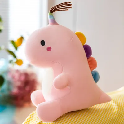 A pink plush dinosaur toy is sitting on a yellow checkered surface, with a blurred background of plants and possibly other decorations.
